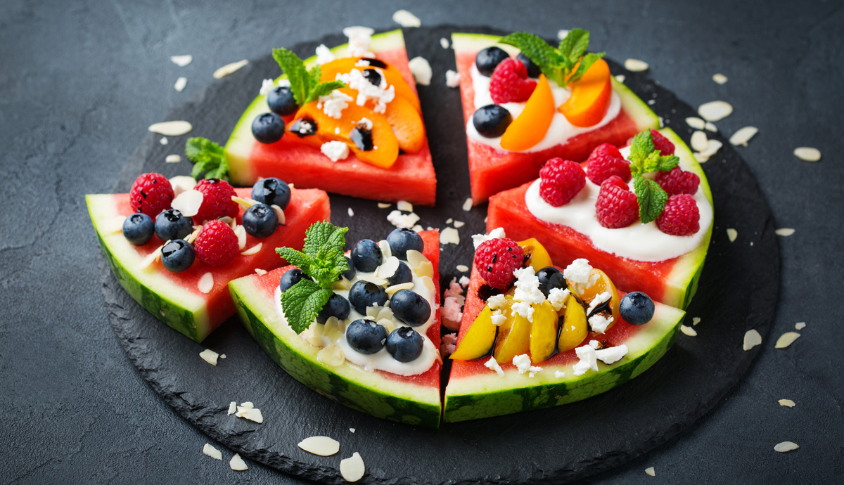 Slices of watermelon in the shape of pizza with yogurt, fruit, and other toppings.
