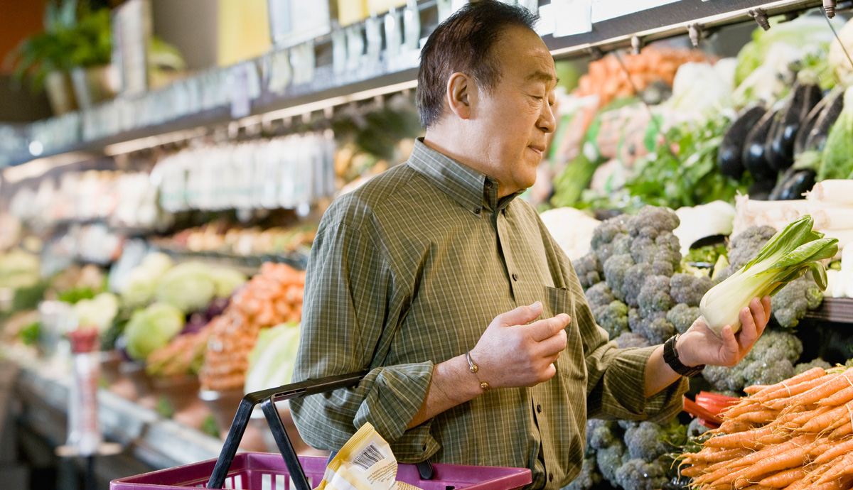 Man holding a basket and bok choy while in produce aisle of grocery store