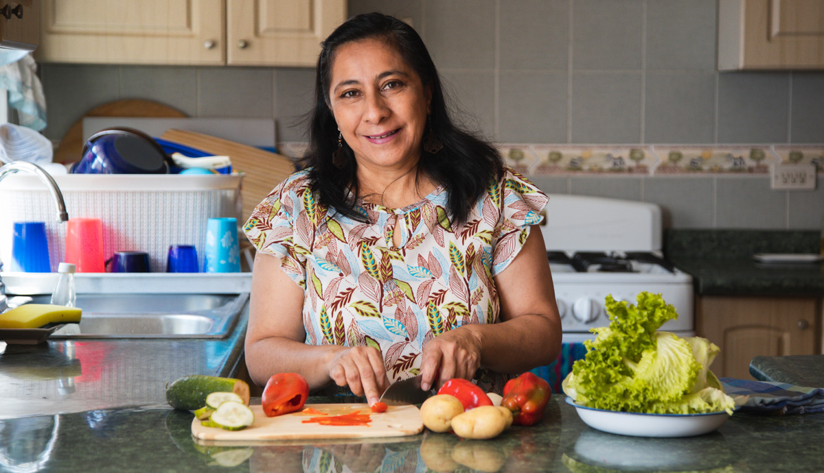 A smiling Latina woman preparing vegetables in her kitchen