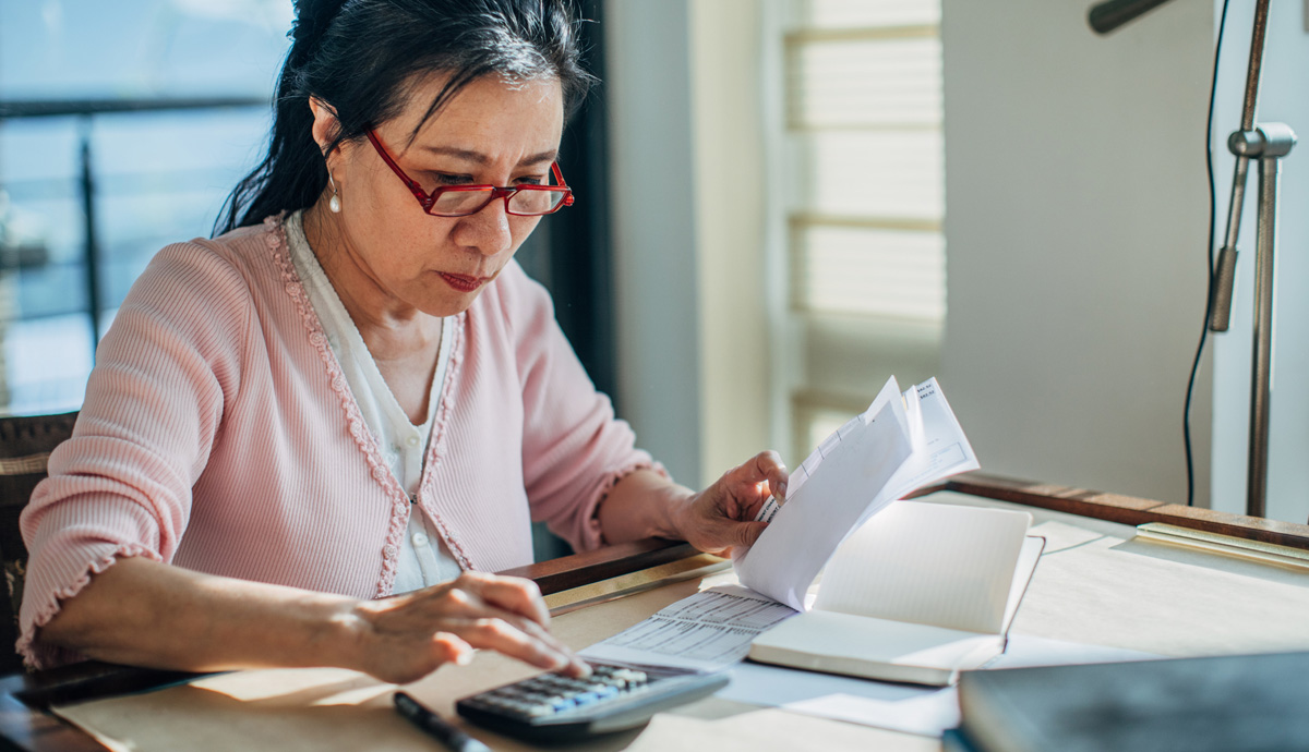 Woman sitting at table holding a check ledger while typing on calculator