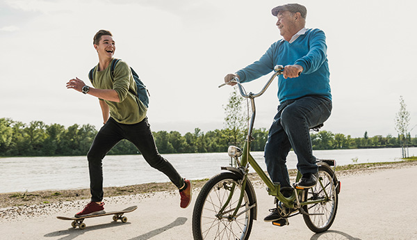 An older man riding a bike and a younger man riding a skateboard enjoying conversation.