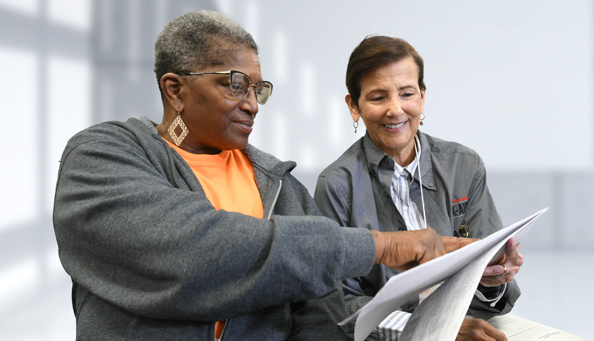 A smiling Tax-Aide volunteer and a woman reviewing a tax document.