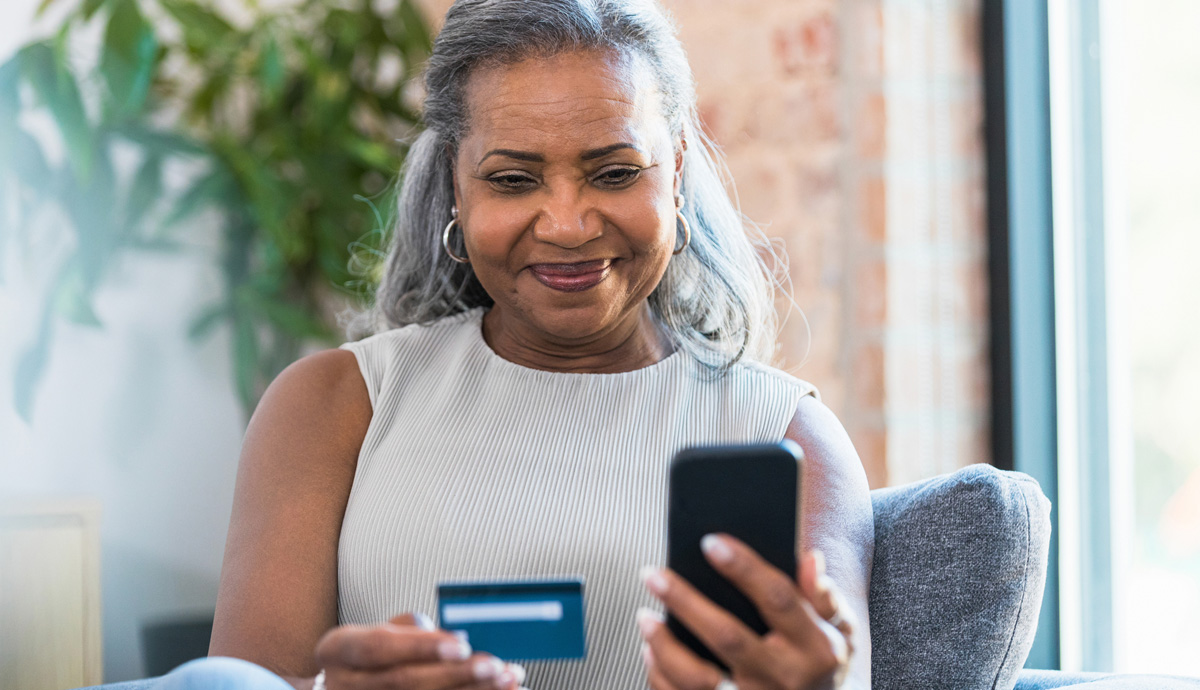 A seated woman holding her credit card and  smartphone.