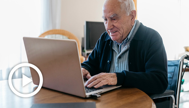 Older man seated at a table working on a laptop