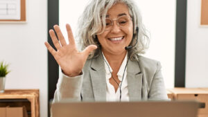 Middle age businesswoman sitting at a desk, communicates using a laptop with a confident smile.
