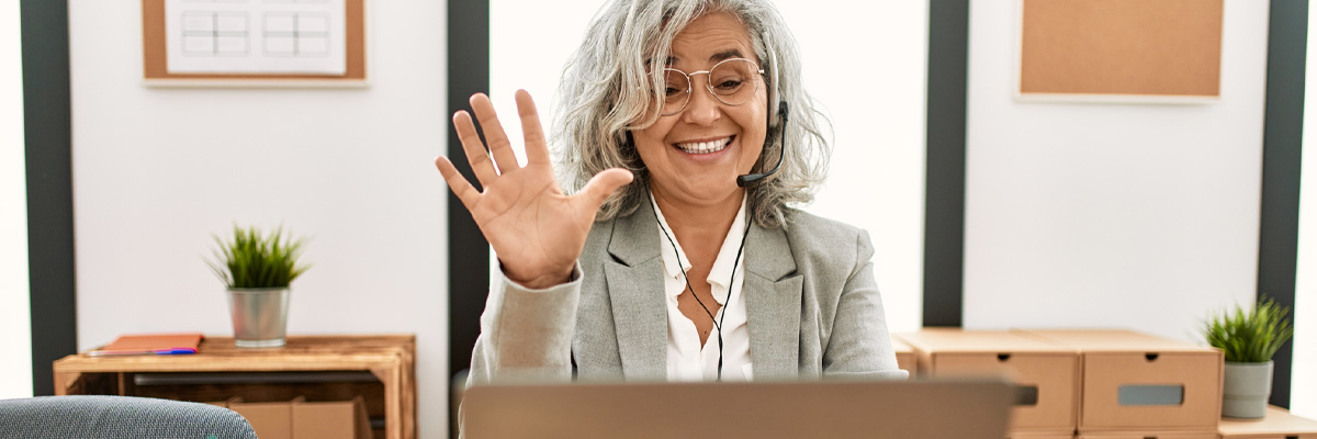 Middle age businesswoman sitting at a desk, communicates using a laptop with a confident smile.