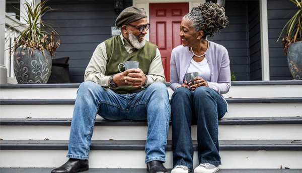A man and woman chat over a cup of coffee while sitting on  front porch steps.