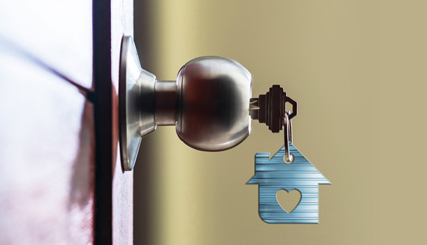 A key on a keychain shaped like a house with a heart on it inserted into a doorknob.