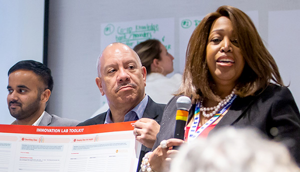 A woman with a microphone stands next to a man holding a poster board related to the Irresistible Offer webinar.