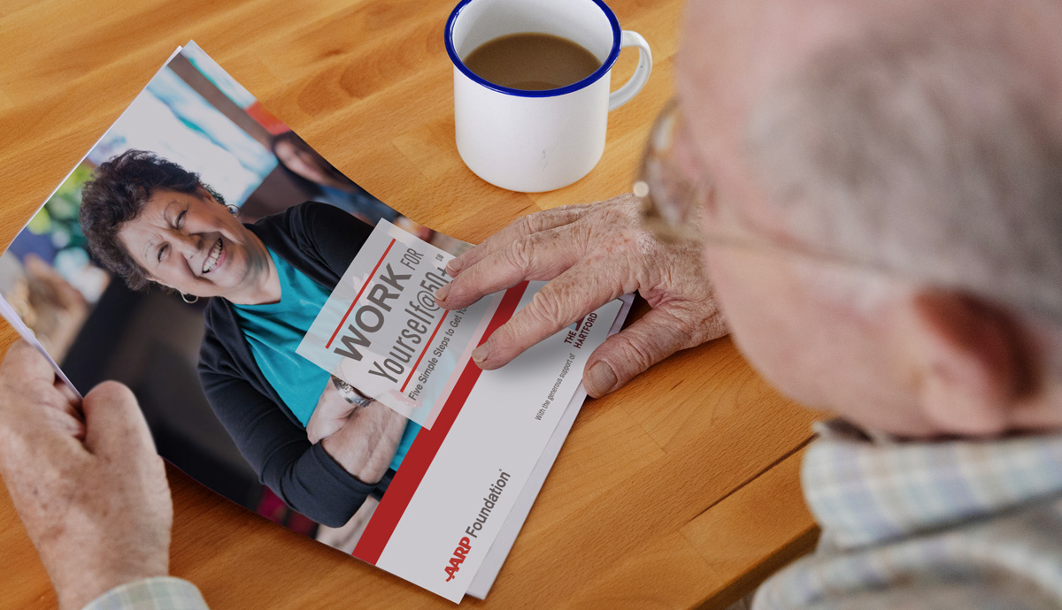 Image of a man sitting at a table holding a printed copy of the Work For Yourself toolkit.