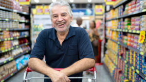 Smiling man leaning on a grocery cart while inside a grocery store.