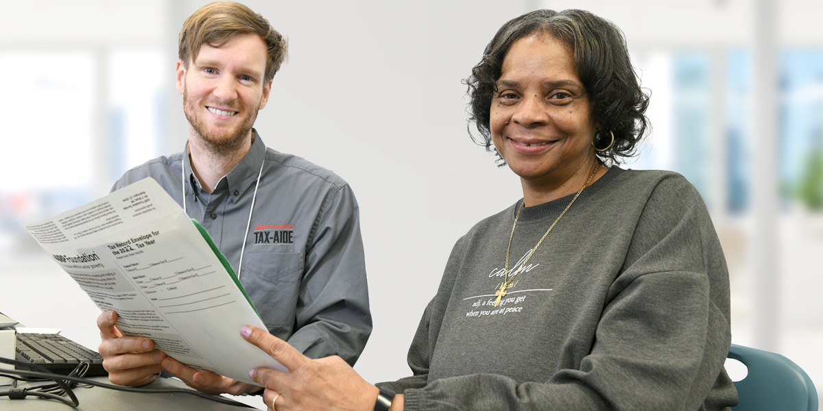 Smiling Tax-Aide volunteer assisting smiling woman with tax paperwork while sitting at table