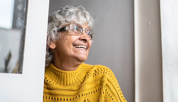 Smiling woman wearing glasses and mustard sweater looking out of window.