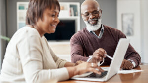 A happy adult couple using a laptop in their living room to look at their financial budgets