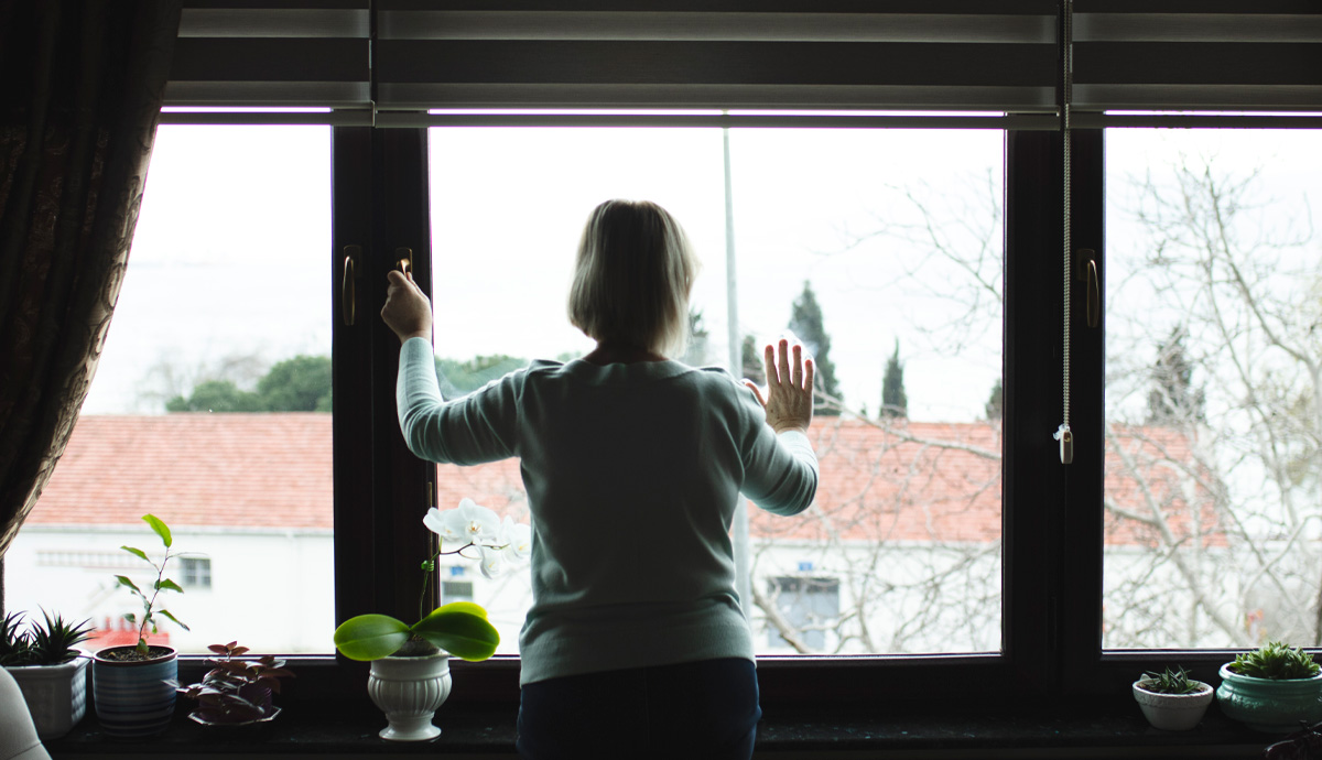 A woman stands in front of a glass window peering out.