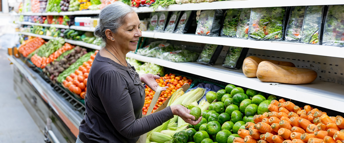 Image of a woman smiling in a grocery store shopping for vegetables