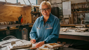Person in a denim shirt, smiling, standing in front of a table in a garage workstation.