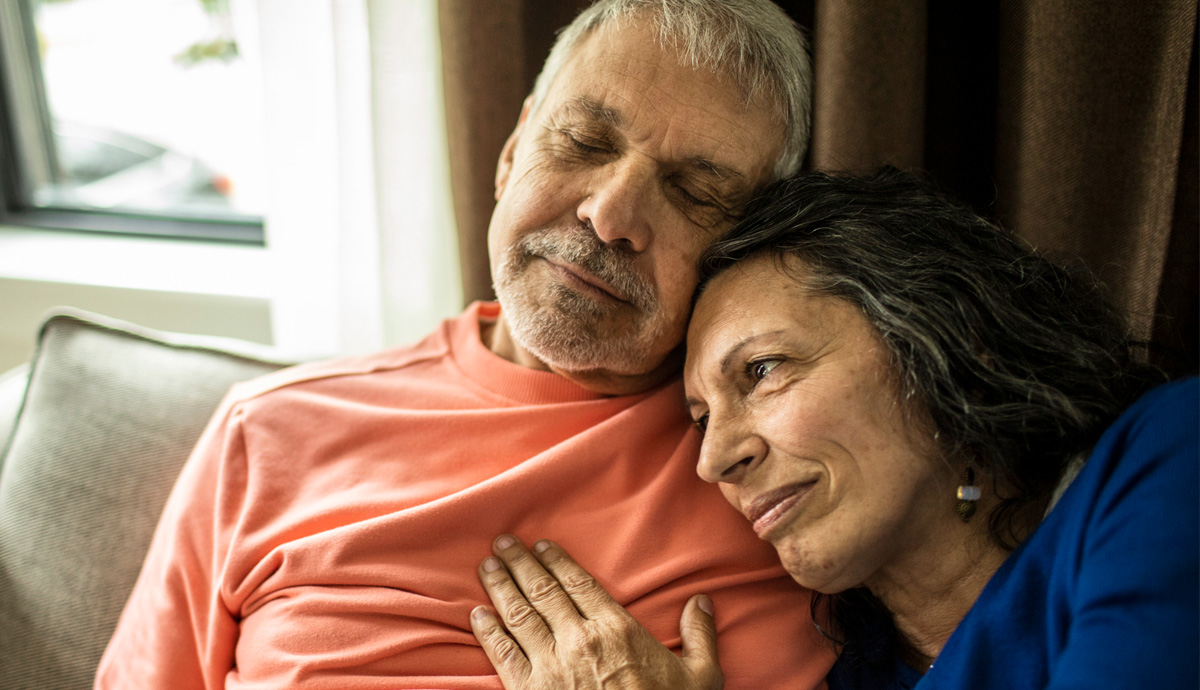 A wife caregiving for her husband lays her head on his shoulder.