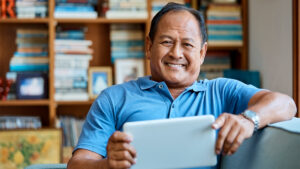 Asian Man sitting on couch, using tablet and smiling