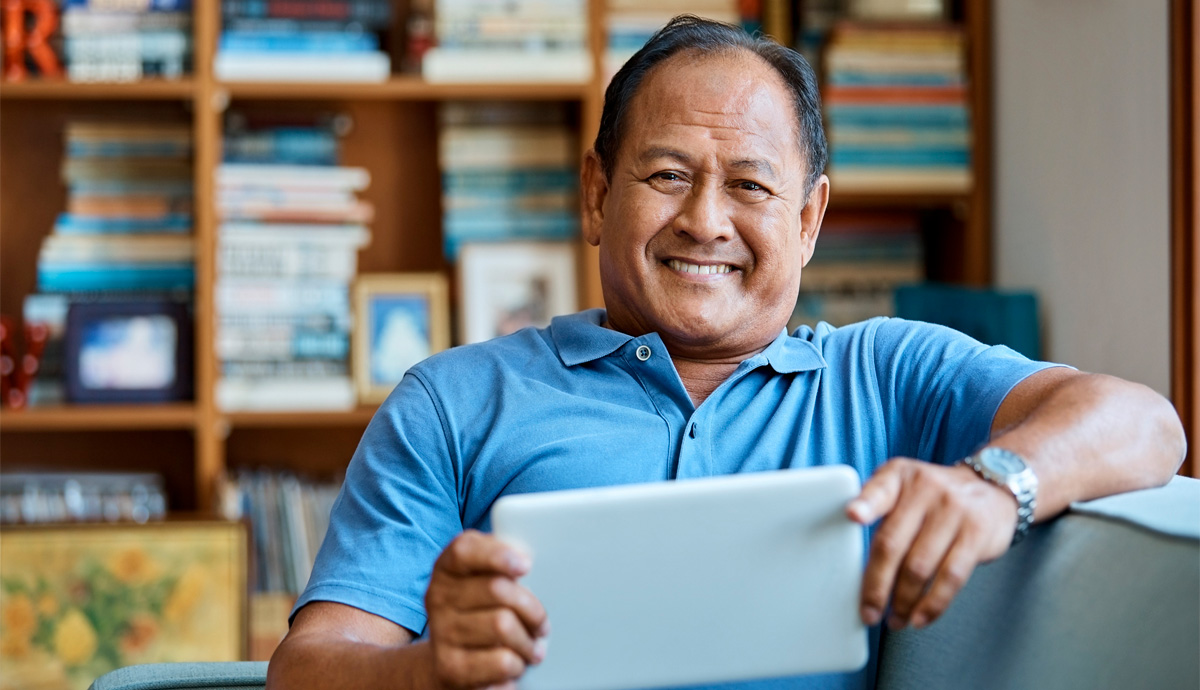 Asian Man sitting on couch, using tablet and smiling