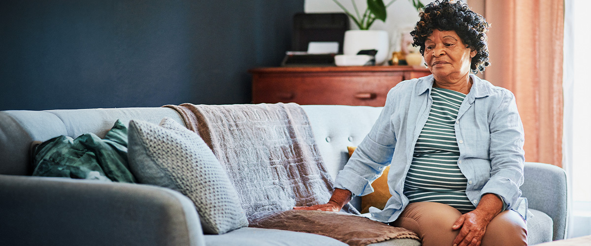 A woman sits alone on a couch staring at the vacant spot beside her.