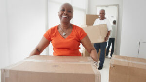 A mature African American woman carrying moving boxes into a new home.