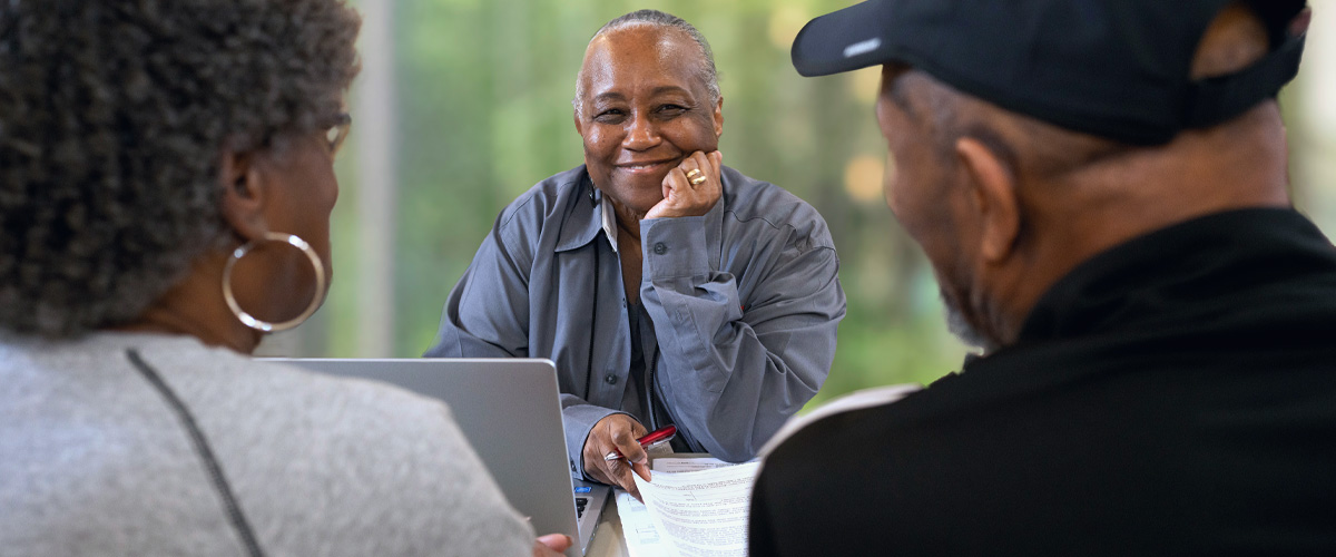 Image of a Tax-Aide volunteer smiling across a table at a couple reviewing tax documents