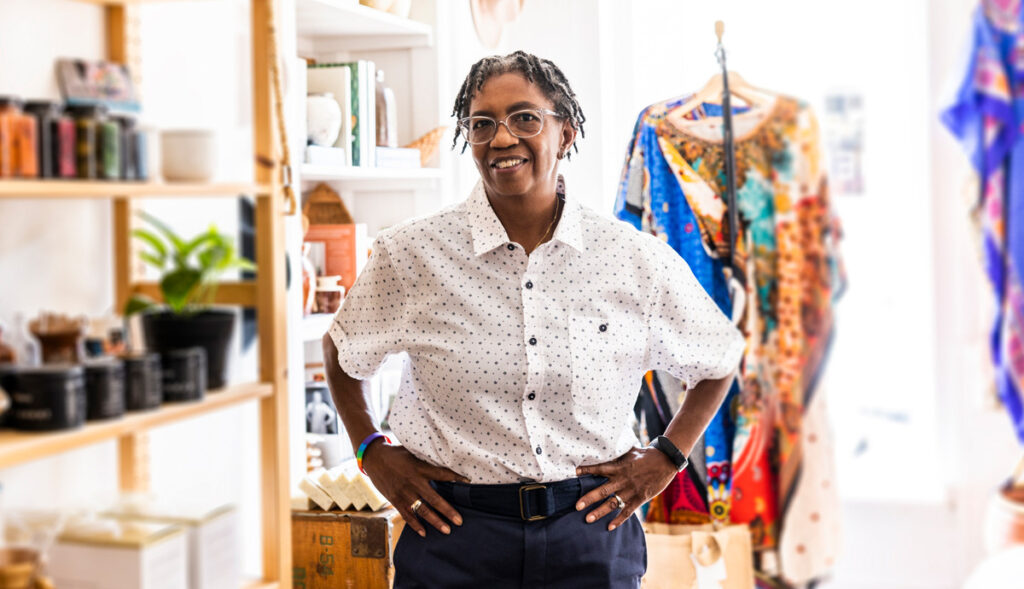 An African American woman stands proudly in the boutique clothing and houseware shop that she runs.