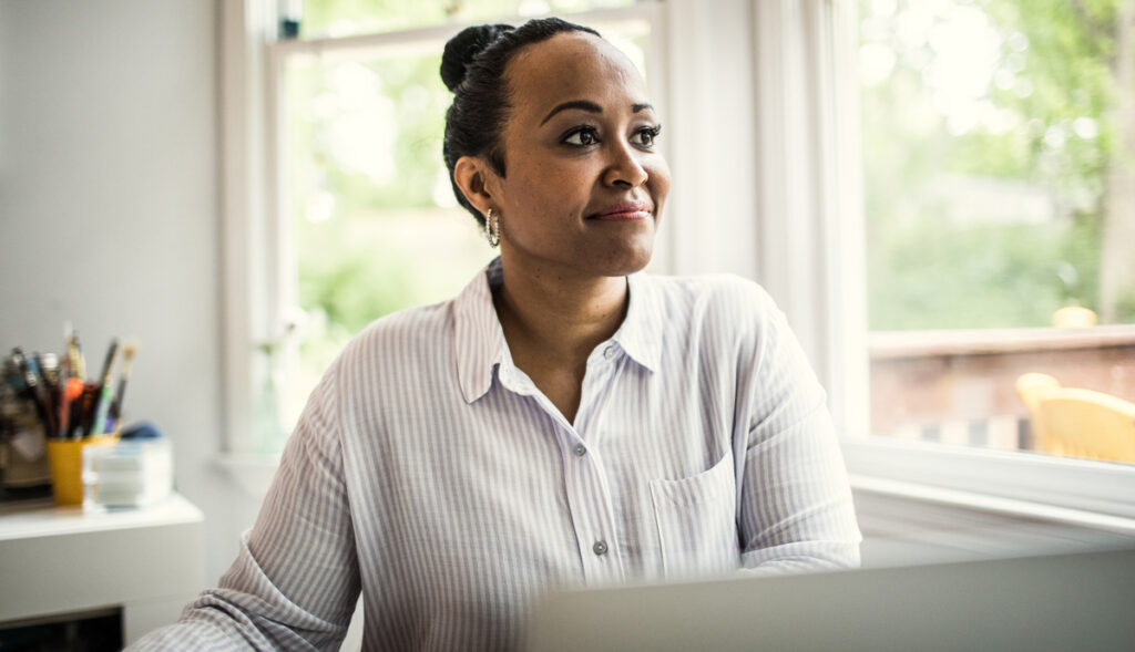 Smiling African American woman wearing white and gray striped shirt sitting at desk with laptop