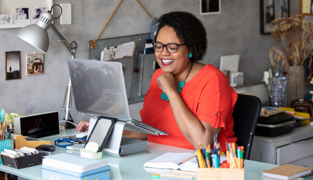 A mature African American woman sits in a creative home office and smiles as she reads from her laptop.