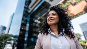 An older professional Black woman in pink blazer smiling confidently in urban setting