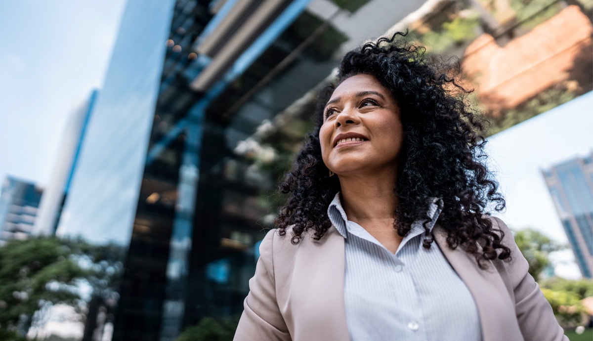 An older professional Black woman in pink blazer smiling confidently in urban setting