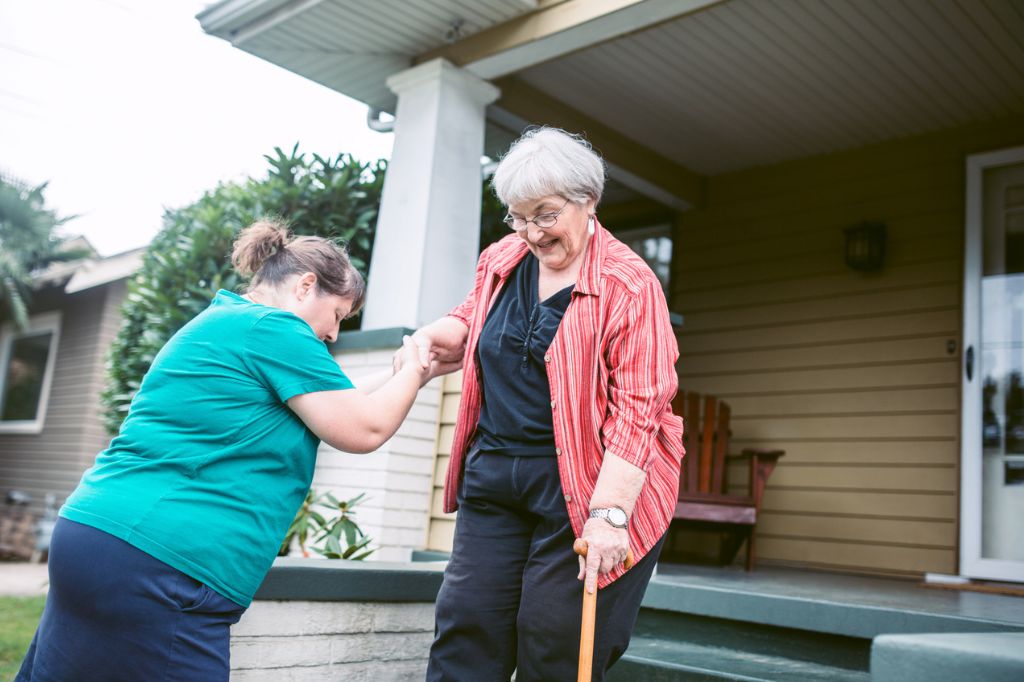 Adult woman in green shirt helping older adult woman in red shirt down the stairs