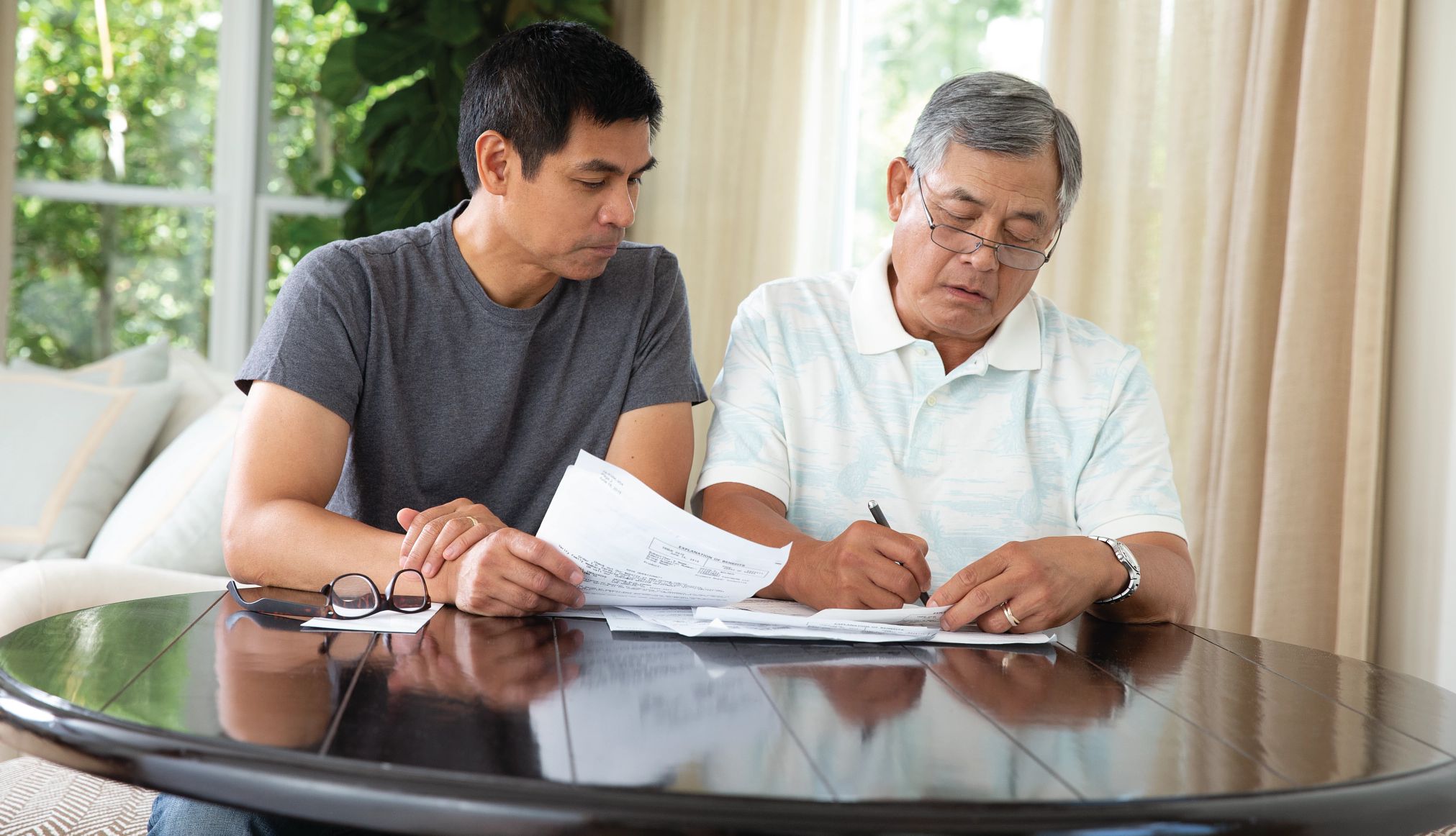 Adult male sitting beside older adult male at a table while looking through paperwork