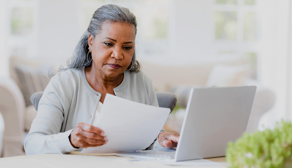 Older adult woman sitting at table looking at student loan bills and laptop