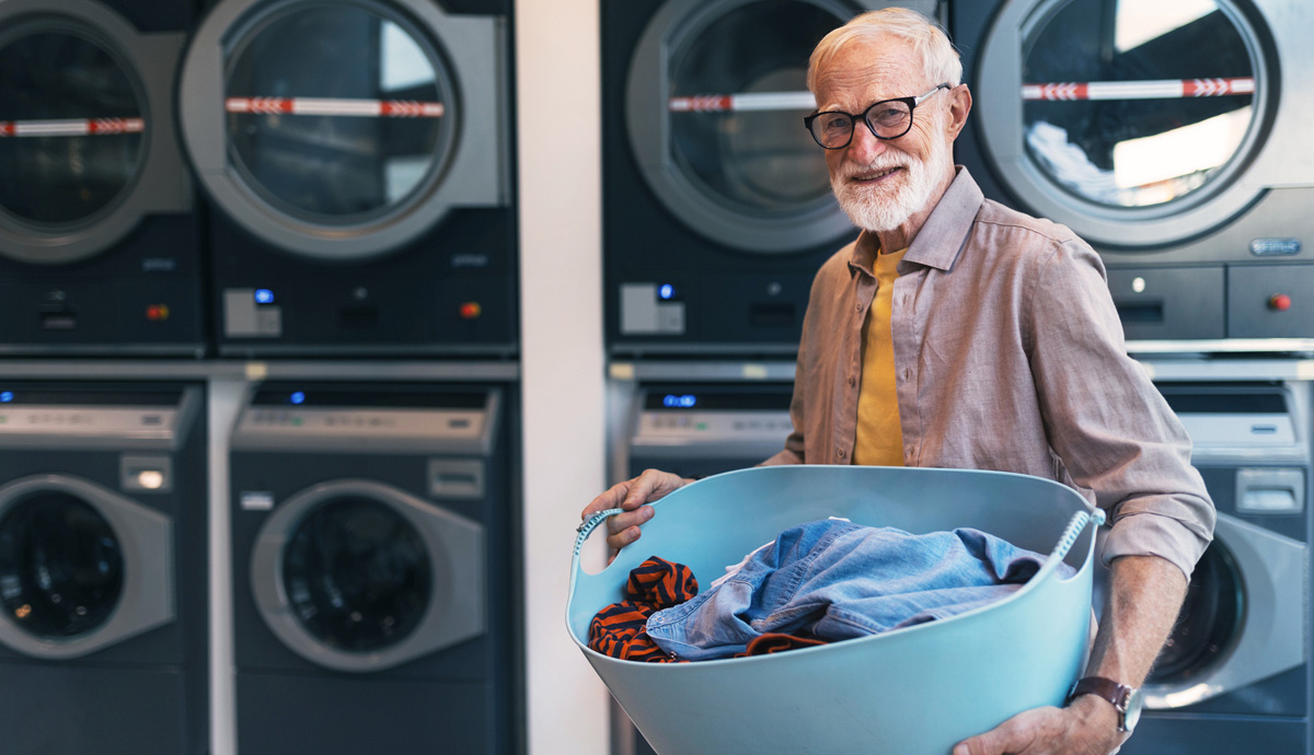 Image of a mature man holding a laundry basket in a laundromat