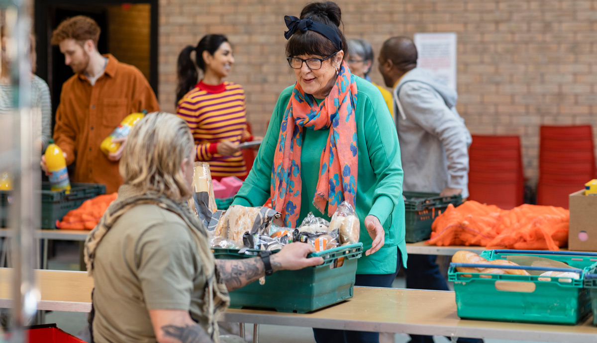 Image of a mature woman in a green shirt and colorful scarf receiving food from a food pantry