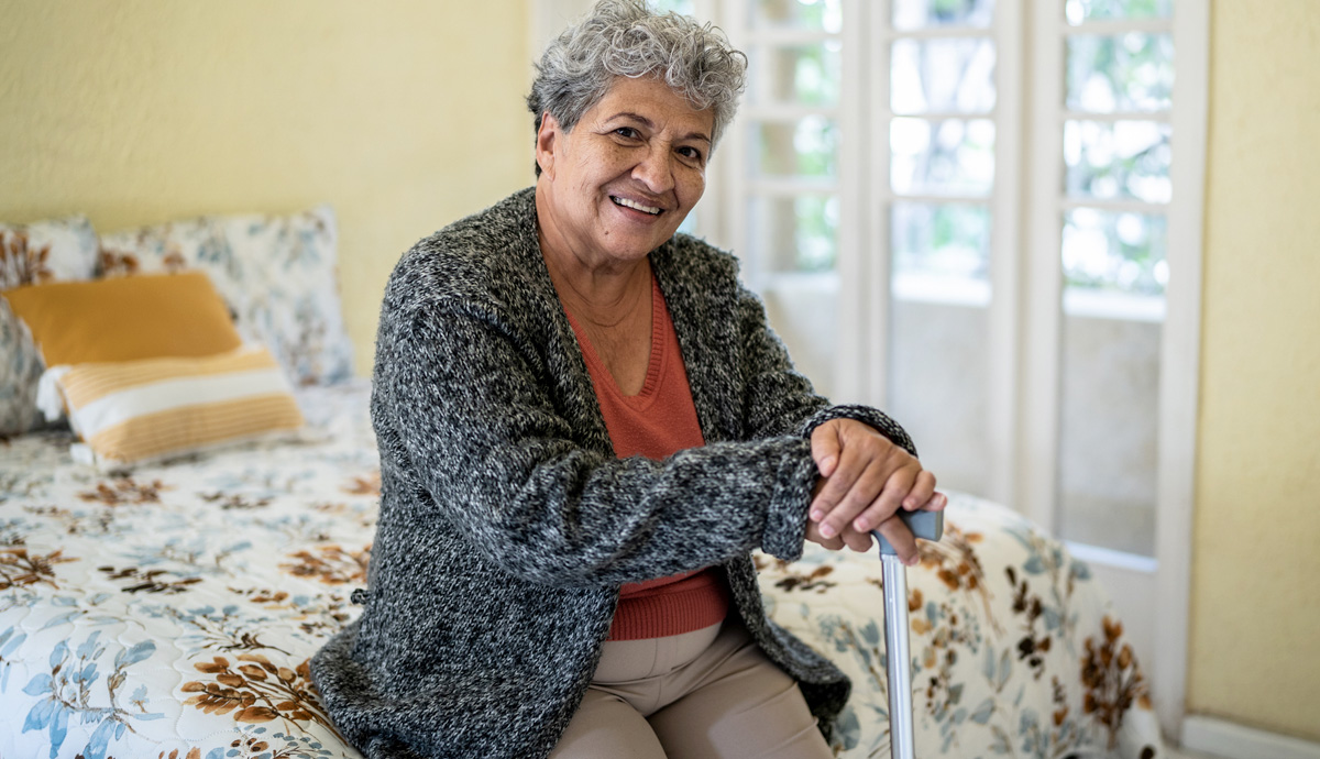 Older woman with a cane smiling while sitting on her bed