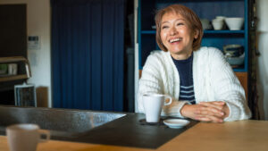 Smiling woman sitting at kitchen table with cup of coffee