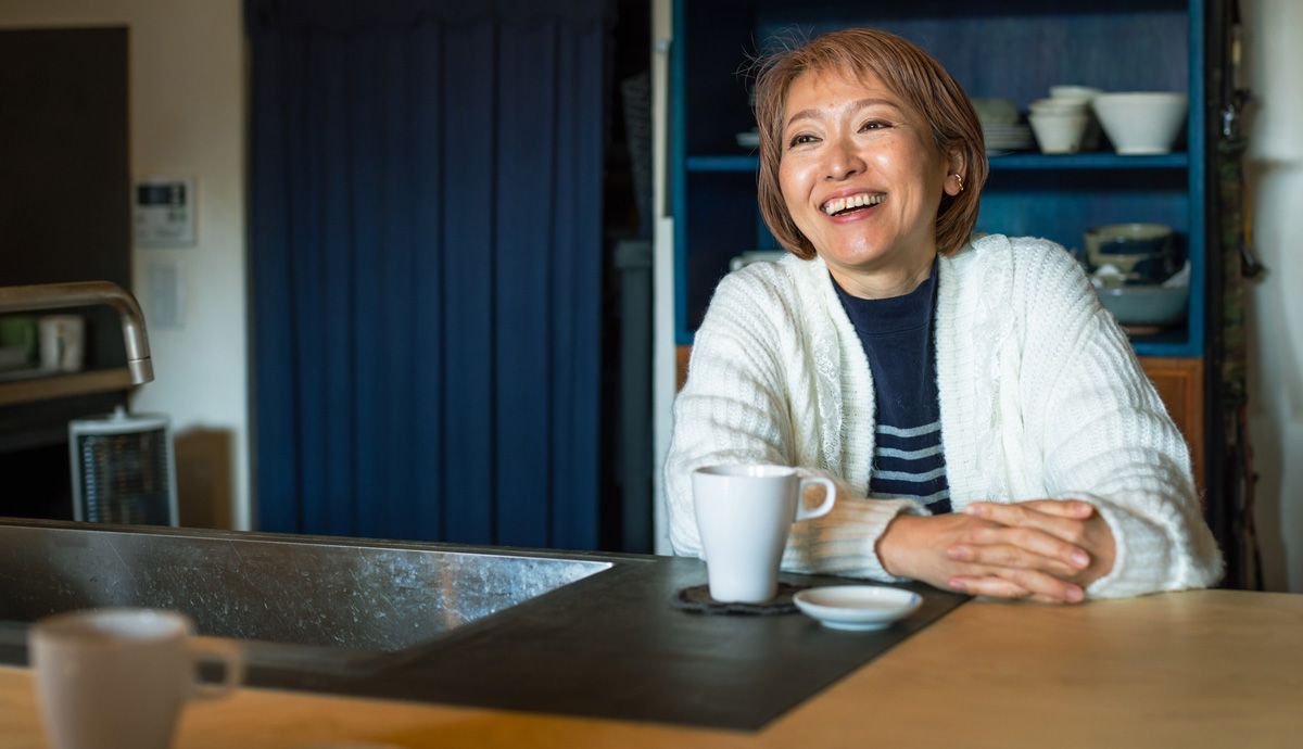 Smiling woman sitting at kitchen table with cup of coffee