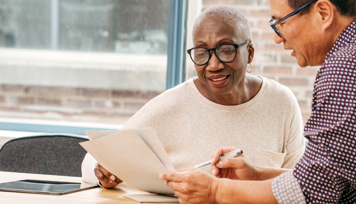 Image of a mature woman in glasses reviewing paperwork with a lawyer.