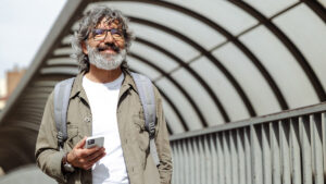 Person with gray hair and beard checking his phone on a city sidewalk