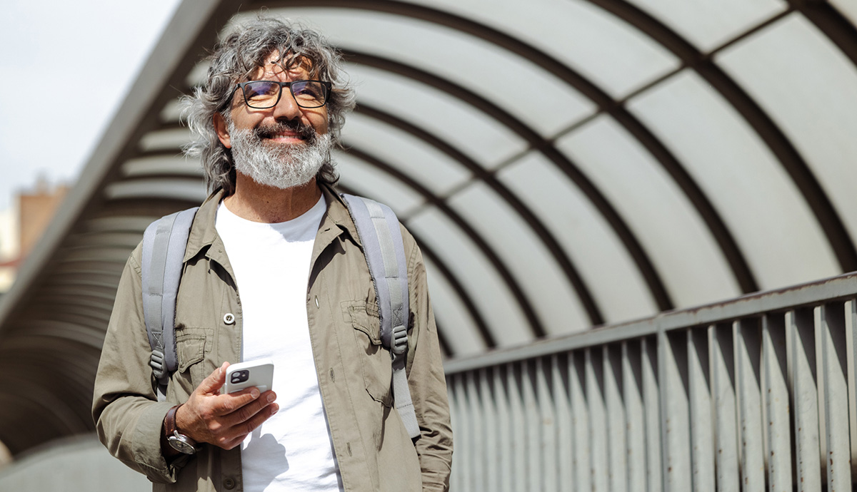 Person with gray hair and beard checking his phone on a city sidewalk